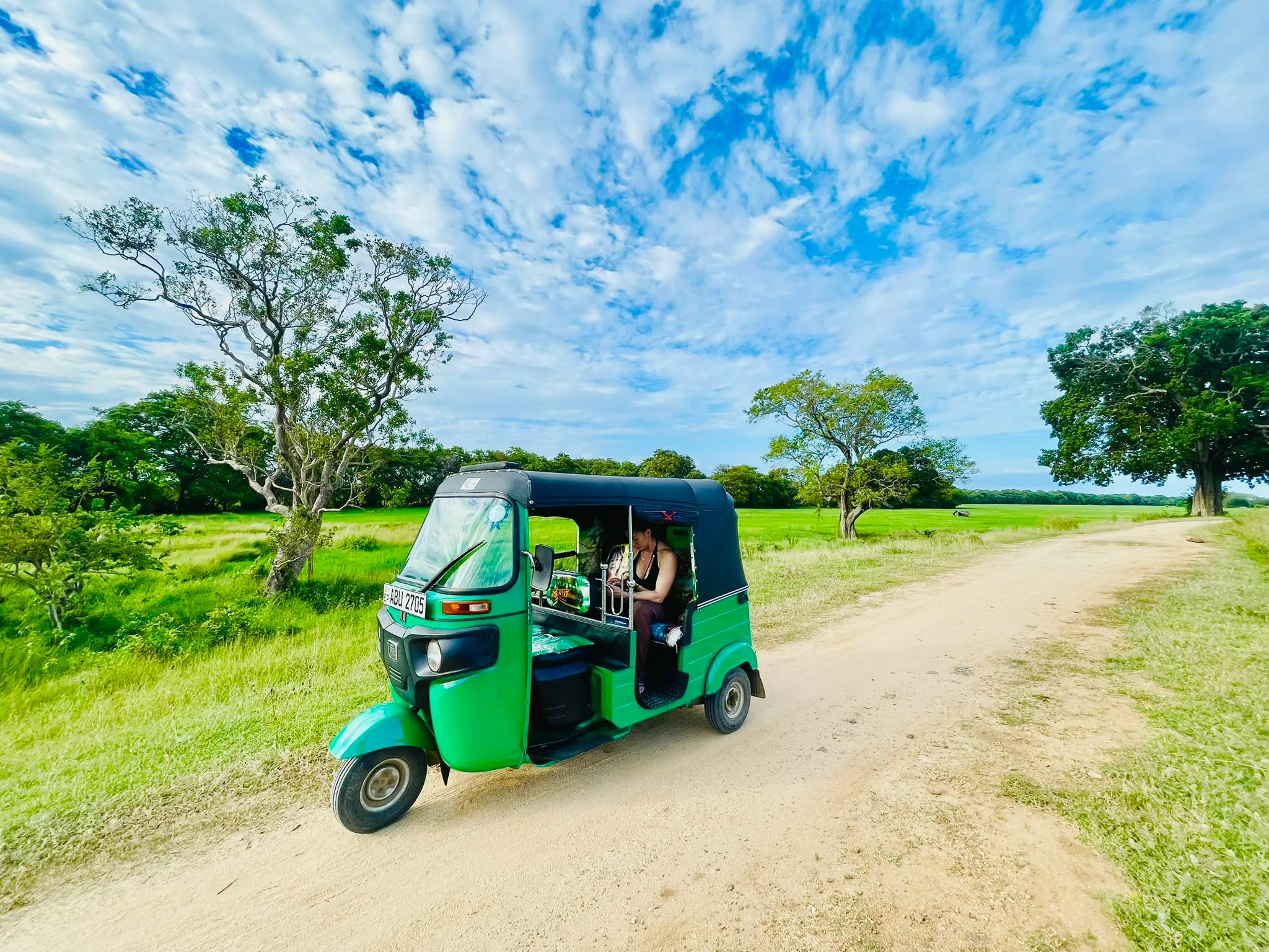 Green RideMe tuk tuk on a scenic road near Arugam Bay under a bright blue sky